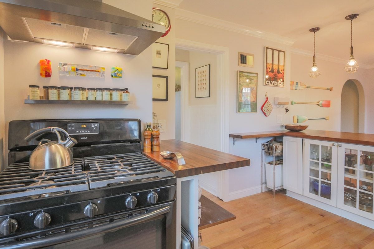 Kitchen with a black gas range, butcher-block counters, and white glass-front cabinets.
