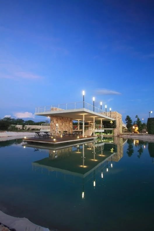 Swimming pool reflecting an illuminated stone pavilion at dusk.
