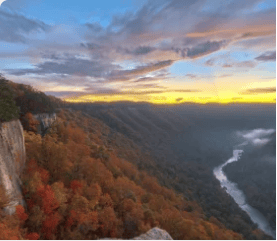 Autumn mountain valley with a winding river and colorful forest at sunset.