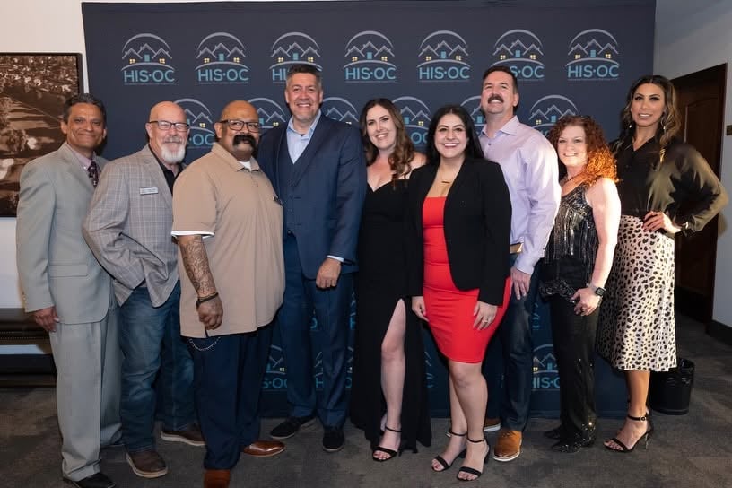 Nine adults pose in front of a HIS'OC backdrop.