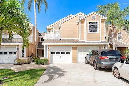Tan two-story townhouse with a garage, parked cars, and palm trees.