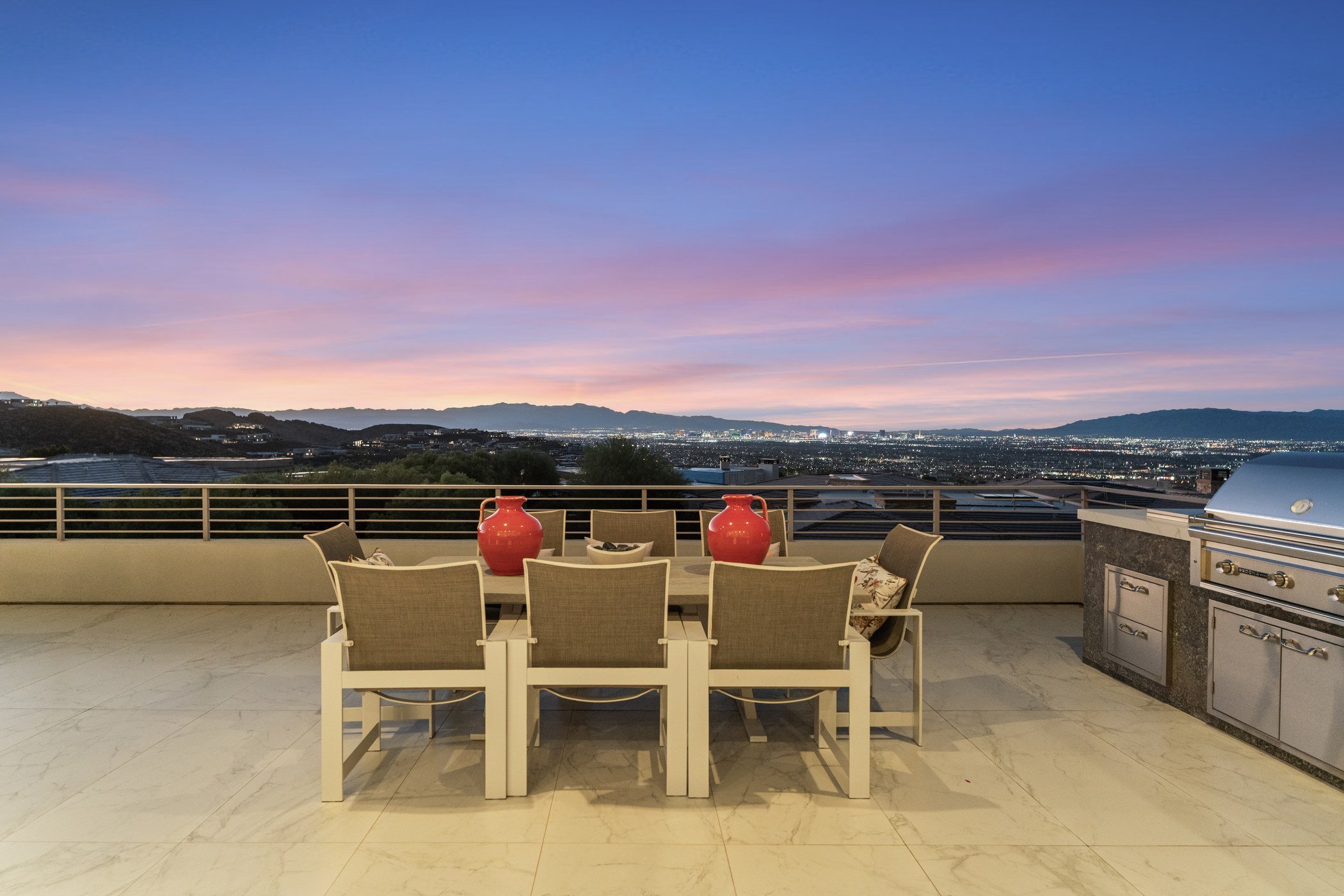 Outdoor dining terrace with a built-in grill overlooking the lit Las Vegas Strip at twilight from a MacDonald Highlands home on Scenic Rim Drive
