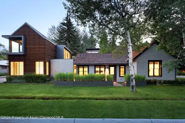 Modern home with wood and gray siding, illuminated windows, and a landscaped lawn.