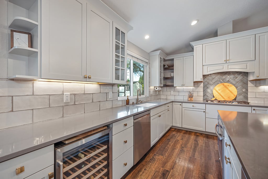 Kitchen with white cabinets, gray counters, tiled backsplash, wine refrigerator, and dark wood floors.