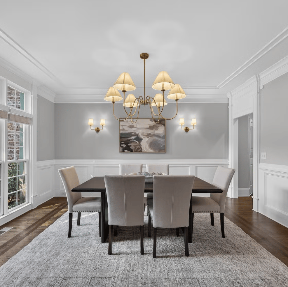 Dining room with upholstered chairs, a brass chandelier, and tall windows.