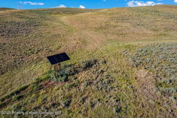 Rolling grassland with a dirt track and a small solar-powered pump.