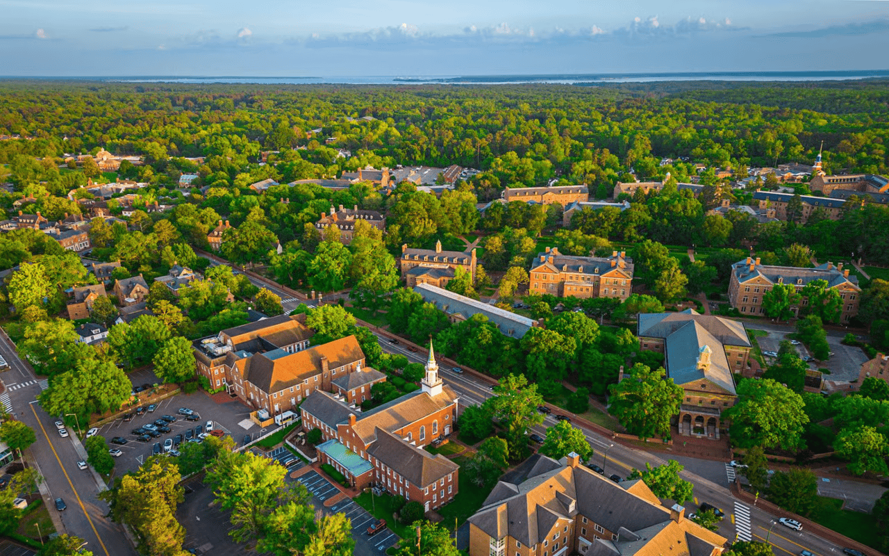 Aerial view of a leafy town with brick buildings, tree-lined roads, and a white church steeple.