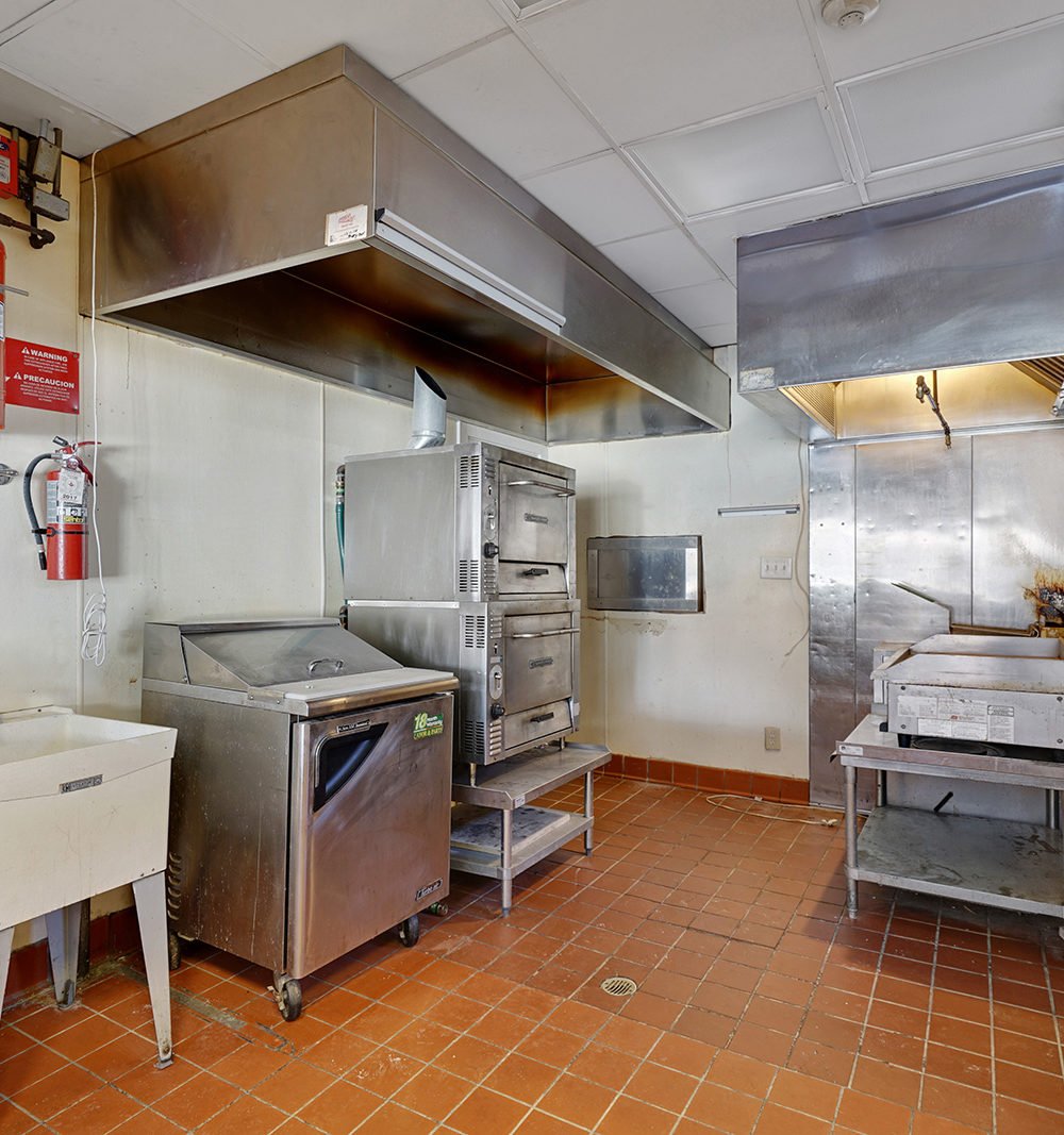 Commercial kitchen with stainless-steel cooking equipment beneath a large ventilation hood.
