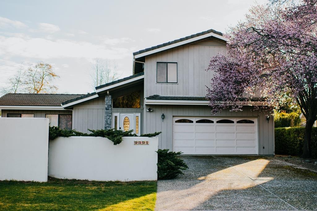 Gray two-story home with a white garage door and flowering pink tree beside the driveway.