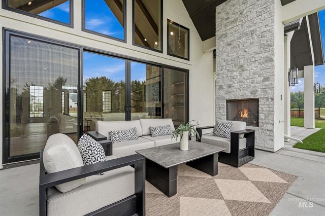 Covered patio with contemporary seating, a tall stone fireplace, and expansive windows.