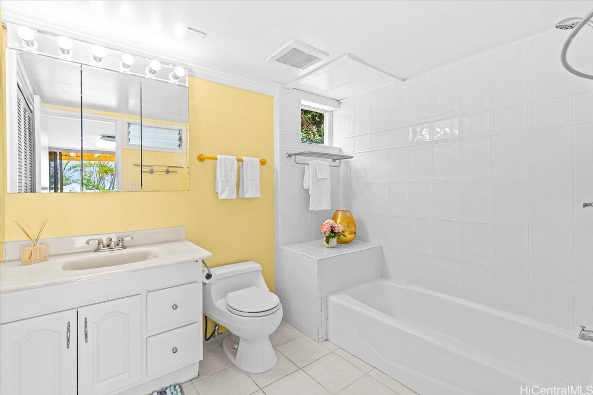 Bathroom with a white vanity, yellow walls, and a tiled bathtub and shower.