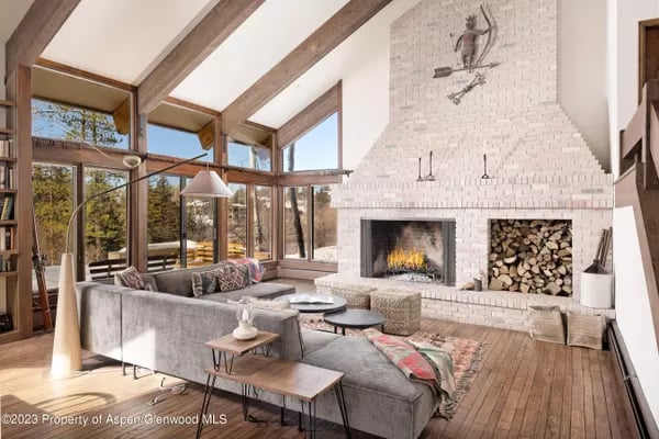 Living room with exposed timber beams, floor-to-ceiling windows, and a large white brick fireplace.