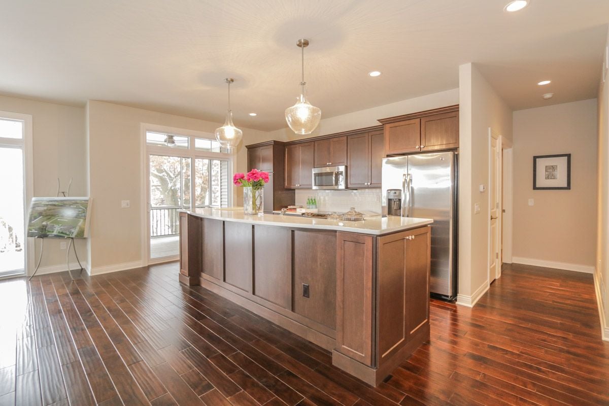 Open kitchen with a large island, dark wood cabinetry, stainless steel appliances, and pendant lights.