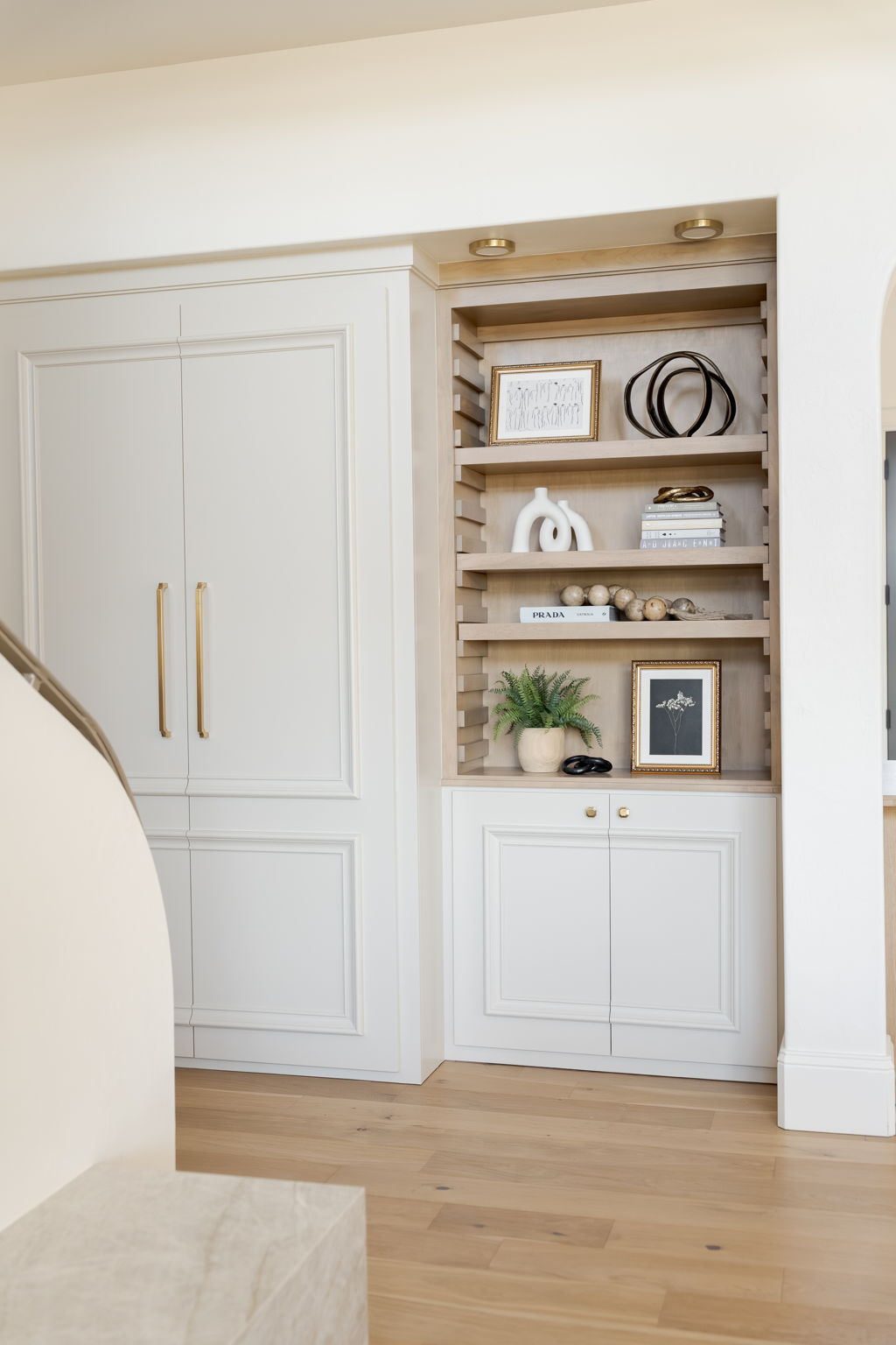 Custom white built-in cabinets with brass handles and styled open wood shelves.