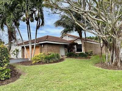 Single-story brick home with a tile roof, broad lawn, and mature palm trees.