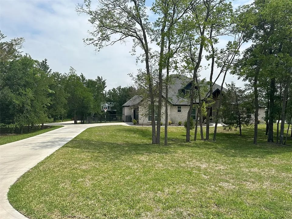 Stone house among mature trees, with a curved driveway and basketball hoop.