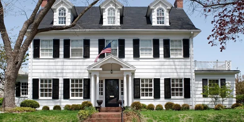 White Colonial-style house with black shutters, three dormers, and a covered front entrance.
