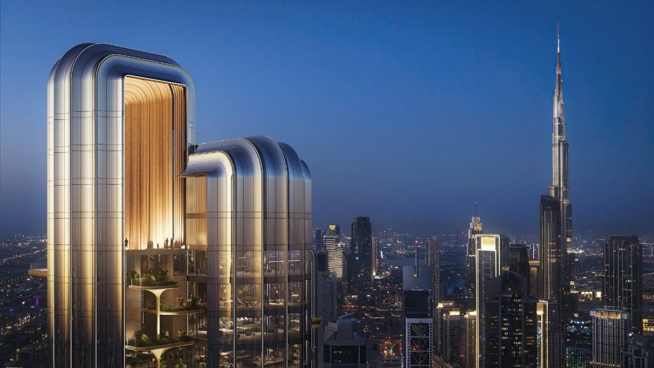 Sculptural high-rise with a rounded metallic façade overlooking the skyline and Burj Khalifa at dusk.