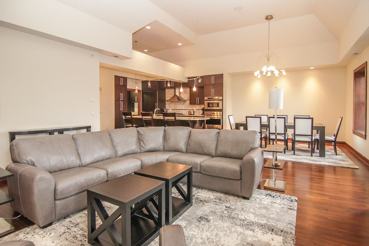 Open-plan living room with a gray sectional, dark kitchen cabinetry, and a vaulted ceiling.