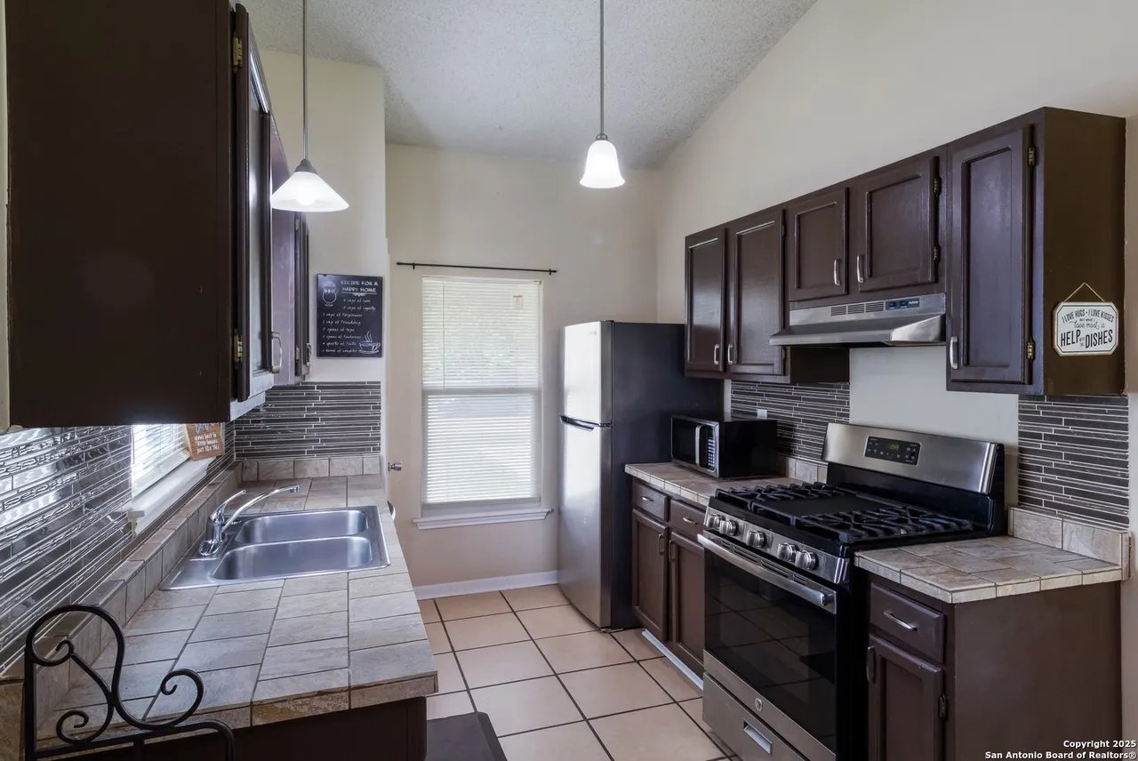 Kitchen with dark wood cabinets, tiled counters, stainless steel gas range, and a double-basin sink.