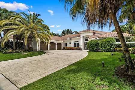 Single-story stucco home with a curved driveway, tiled roof, and mature palms.