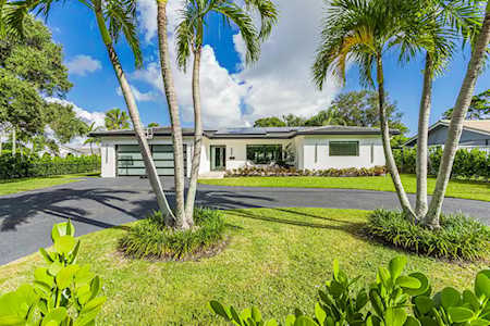 Modern single-story home framed by tall palms, with a broad lawn and driveway.