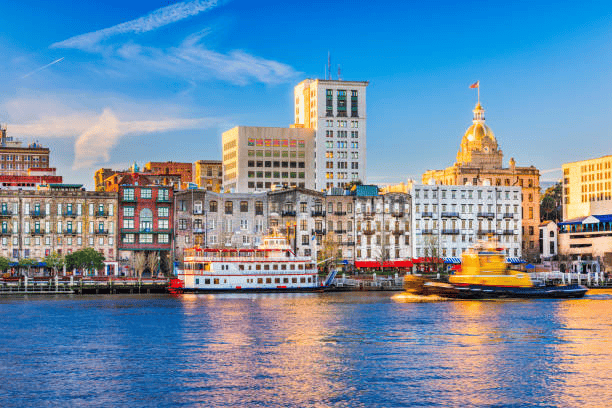Savannah waterfront with historic buildings, a riverboat, and the golden-domed City Hall.