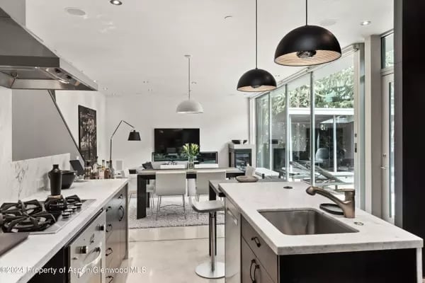 Modern kitchen with a large white island, pendant lights, and floor-to-ceiling windows.