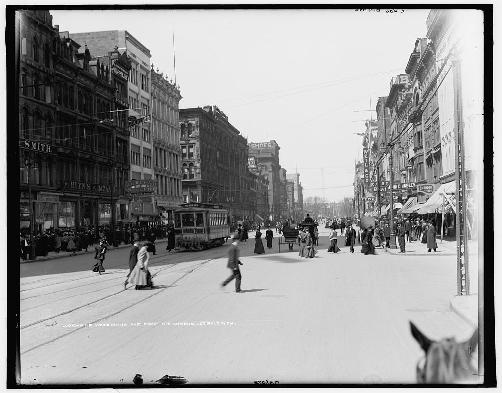 Historic Woodward Avenue in Detroit, with a streetcar, pedestrians, and horse-drawn vehicles.