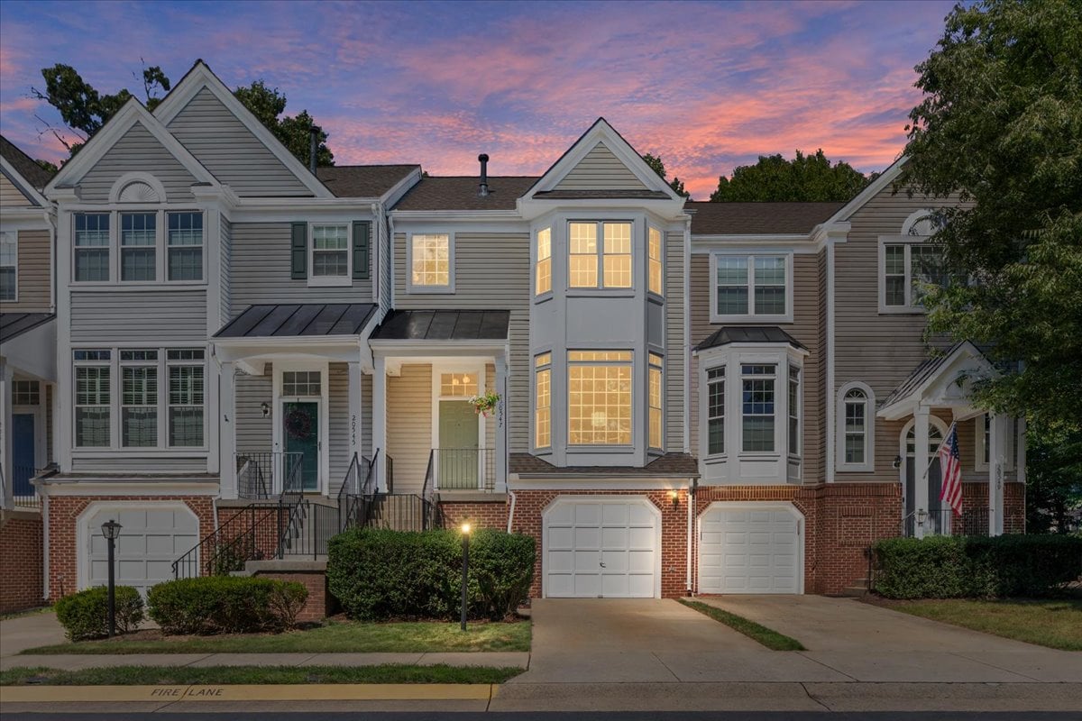 Attached townhome with a brick facade, bay windows, and glowing interior lights at dusk.