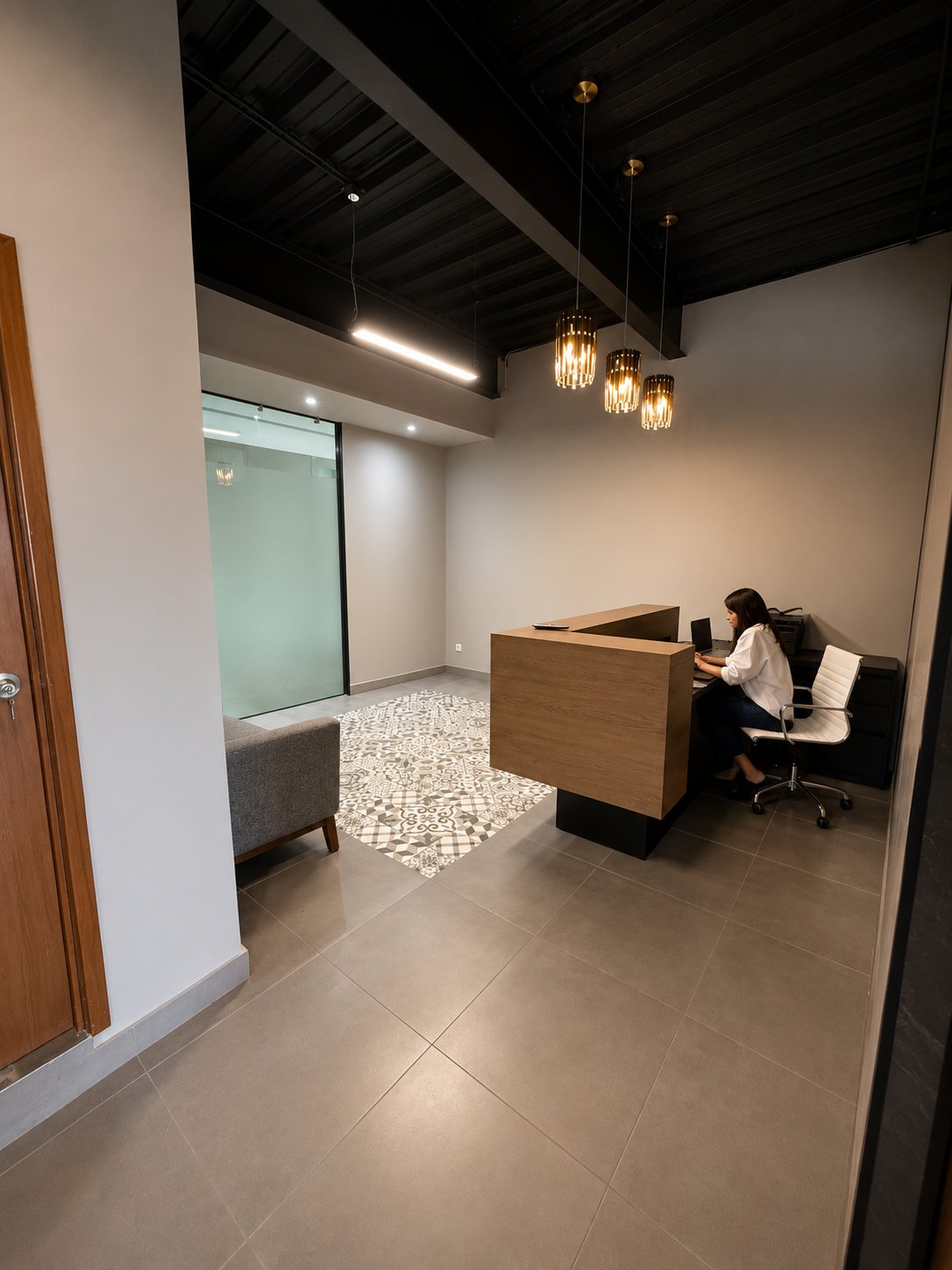 Office reception with a wooden desk, glass partition, patterned tile accent, and pendant lights.