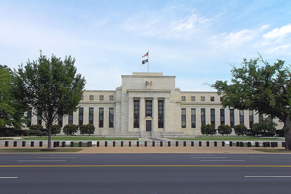 Marriner S. Eccles Federal Reserve headquarters on Constitution Avenue, Washington, DC, neoclassical marble facade with flags, trees and blue sky.