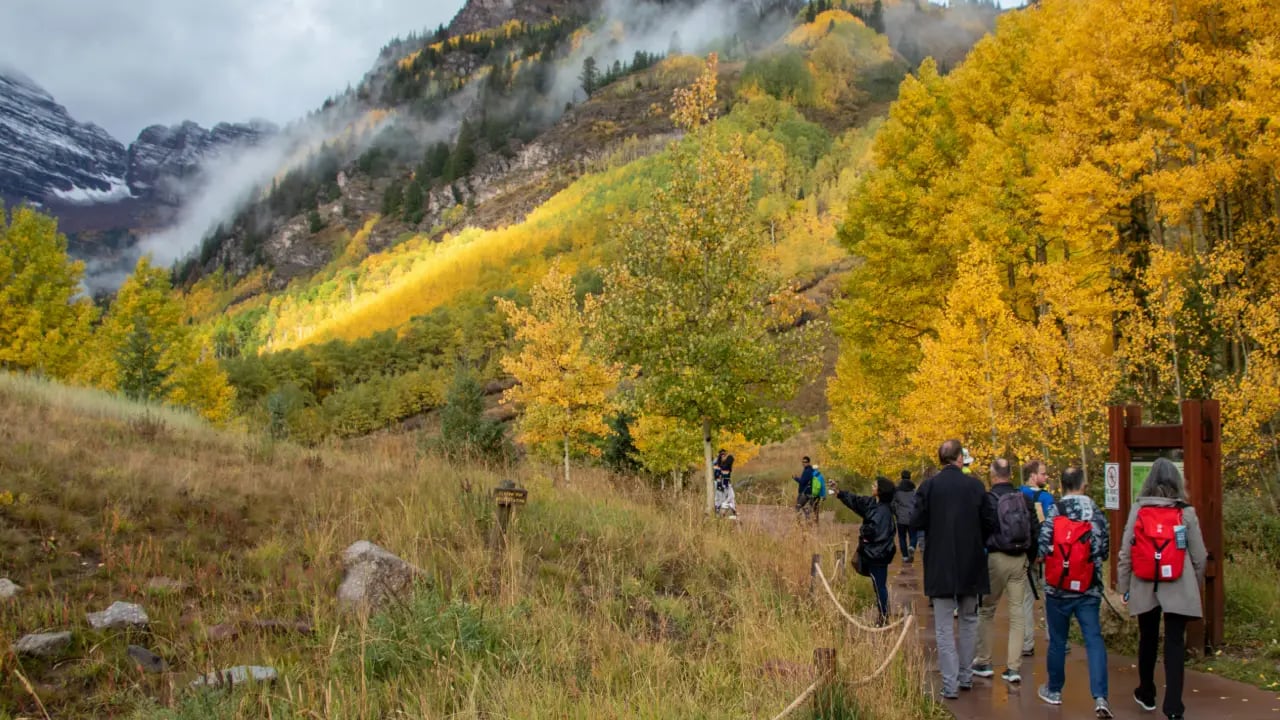 Group of hikers walking through golden fall foliage and mountain views while hiking in Aspen during peak autumn season.