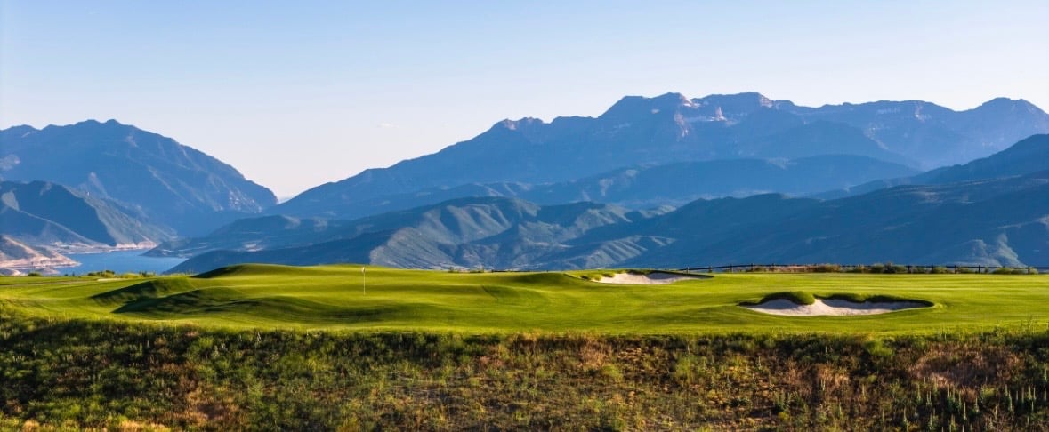 Green golf course with sand bunkers, backed by a wide mountain range.