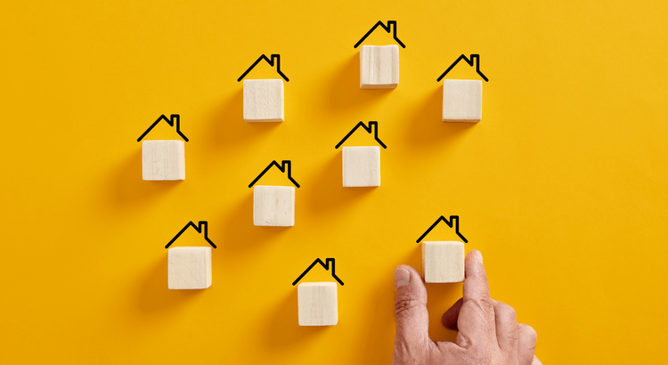 A hand pointing towards a yellow wall adorned with several houses in various colors and styles.