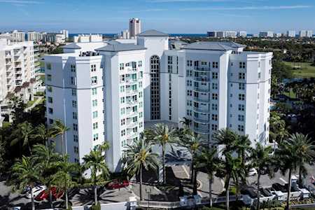 White condominium tower framed by palm trees, with the ocean visible beyond it.