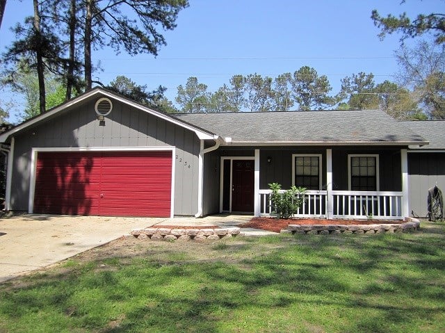 A charming home featuring a red garage and a welcoming front porch, surrounded by a well-maintained yard.