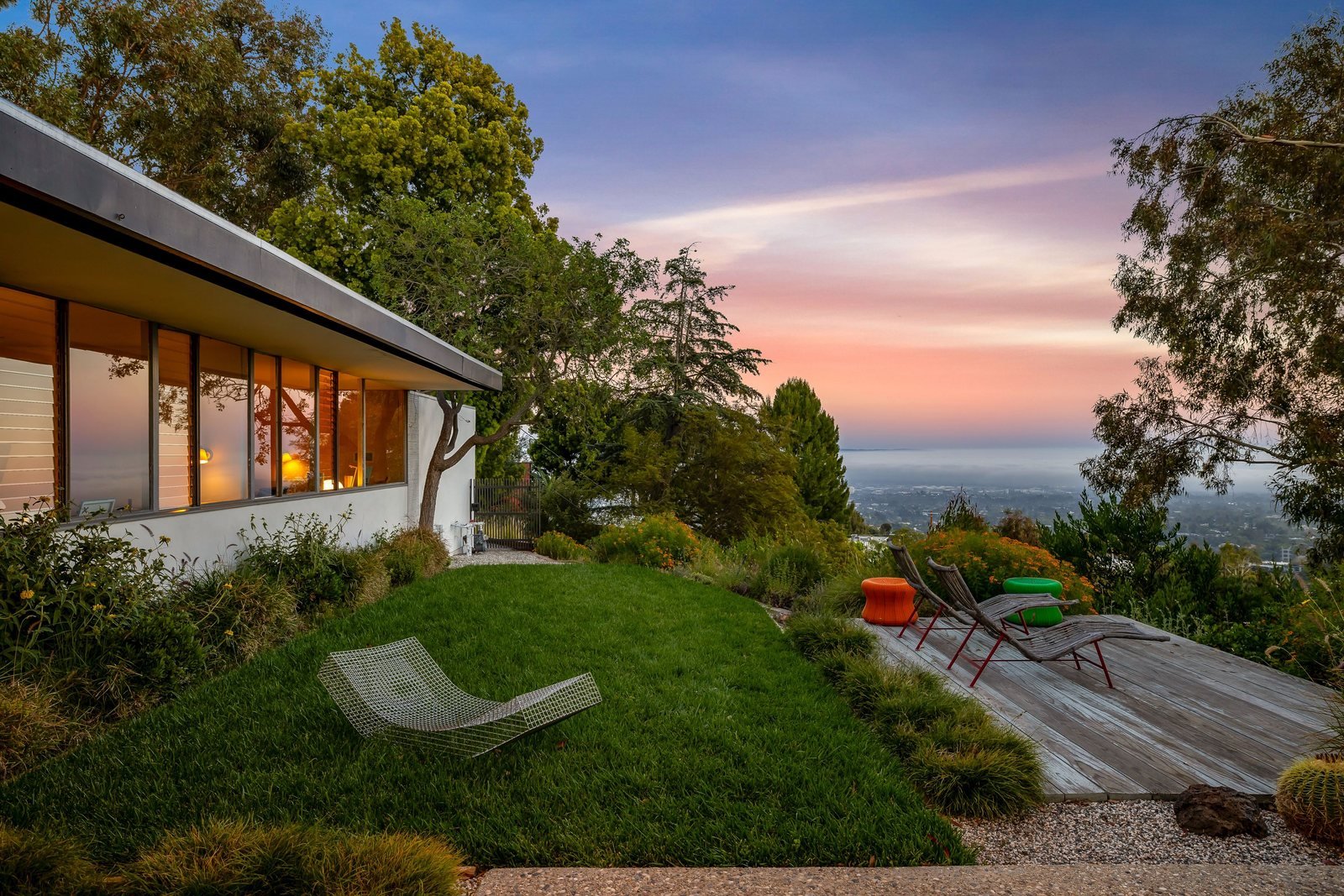 The Sale House at dusk, its glass walls lit from within, with the Los Angeles basin beyond.