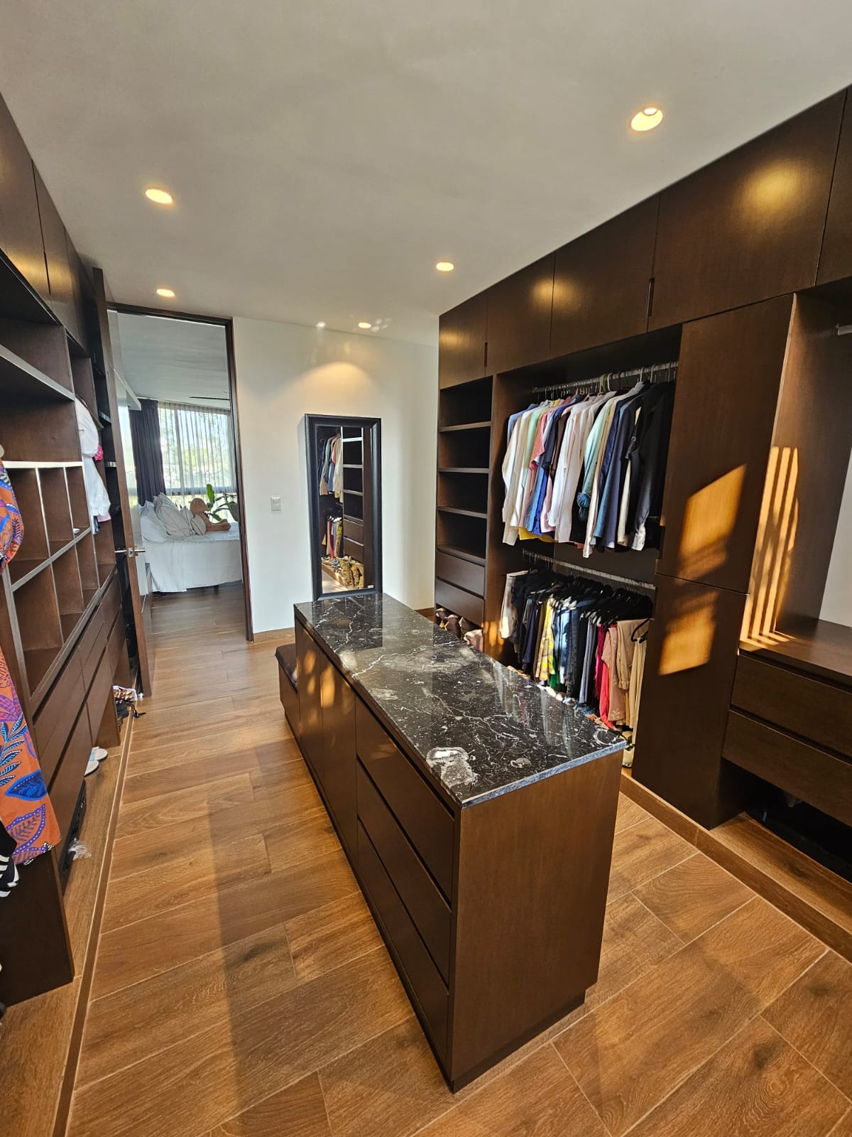 Walk-in closet with dark wood cabinetry, clothes on open rails, and a central stone-topped island.