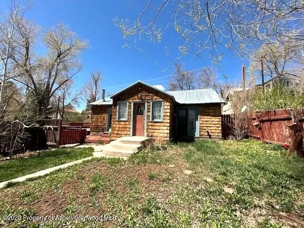 Small shingle-sided home with a metal roof, concrete front steps, and a fenced yard.