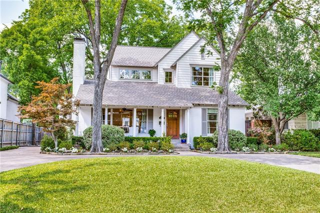White two-story house with a covered porch, mature trees, and a broad lawn.