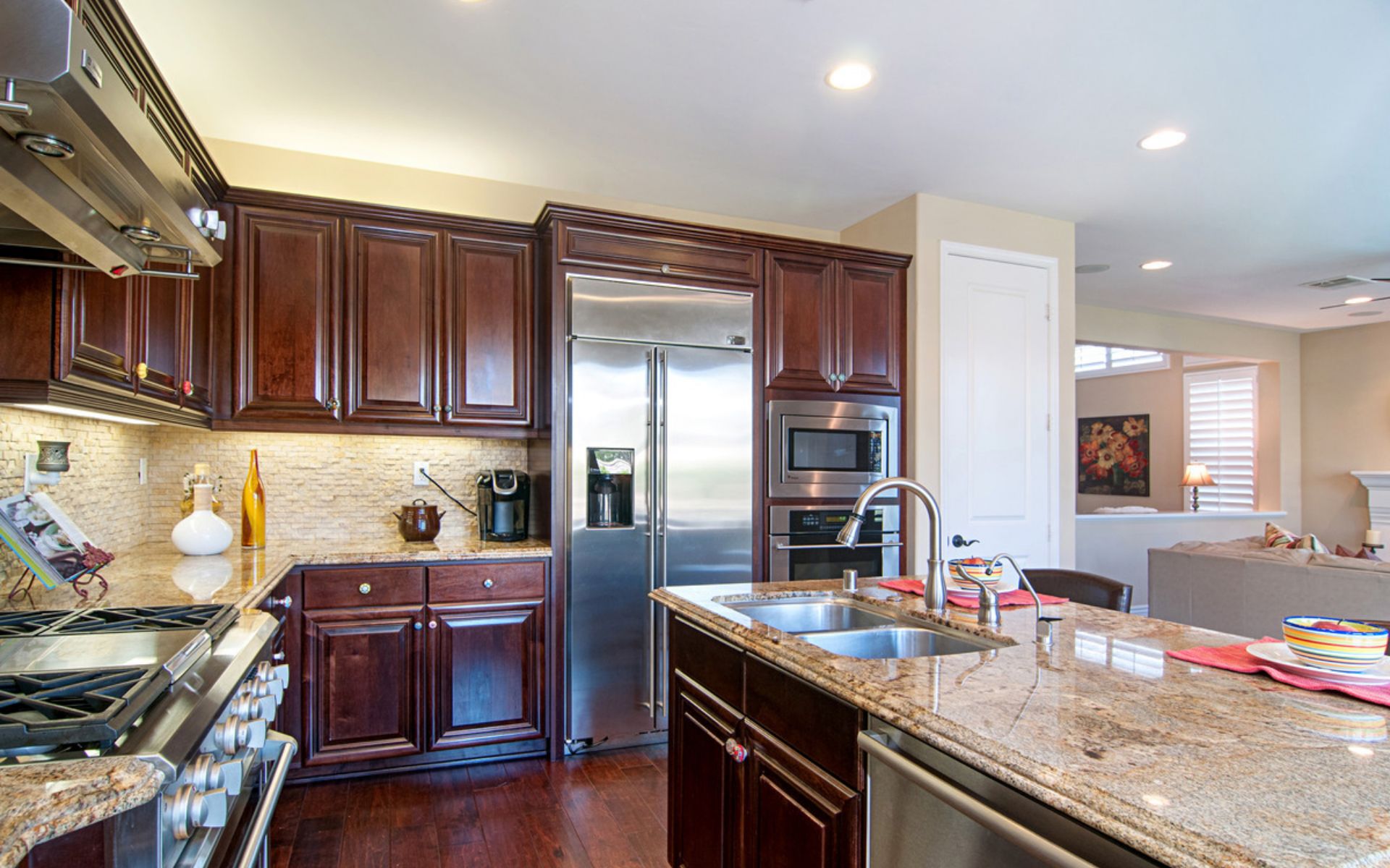 Kitchen with dark wood cabinetry, granite counters, stainless appliances, and a large island sink.