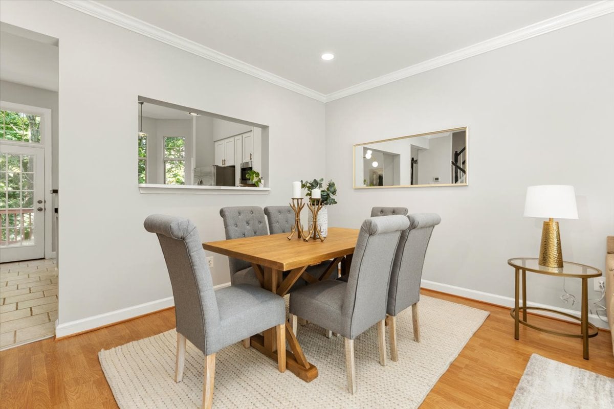 Dining room with a wooden table, gray upholstered chairs, and a kitchen pass-through.