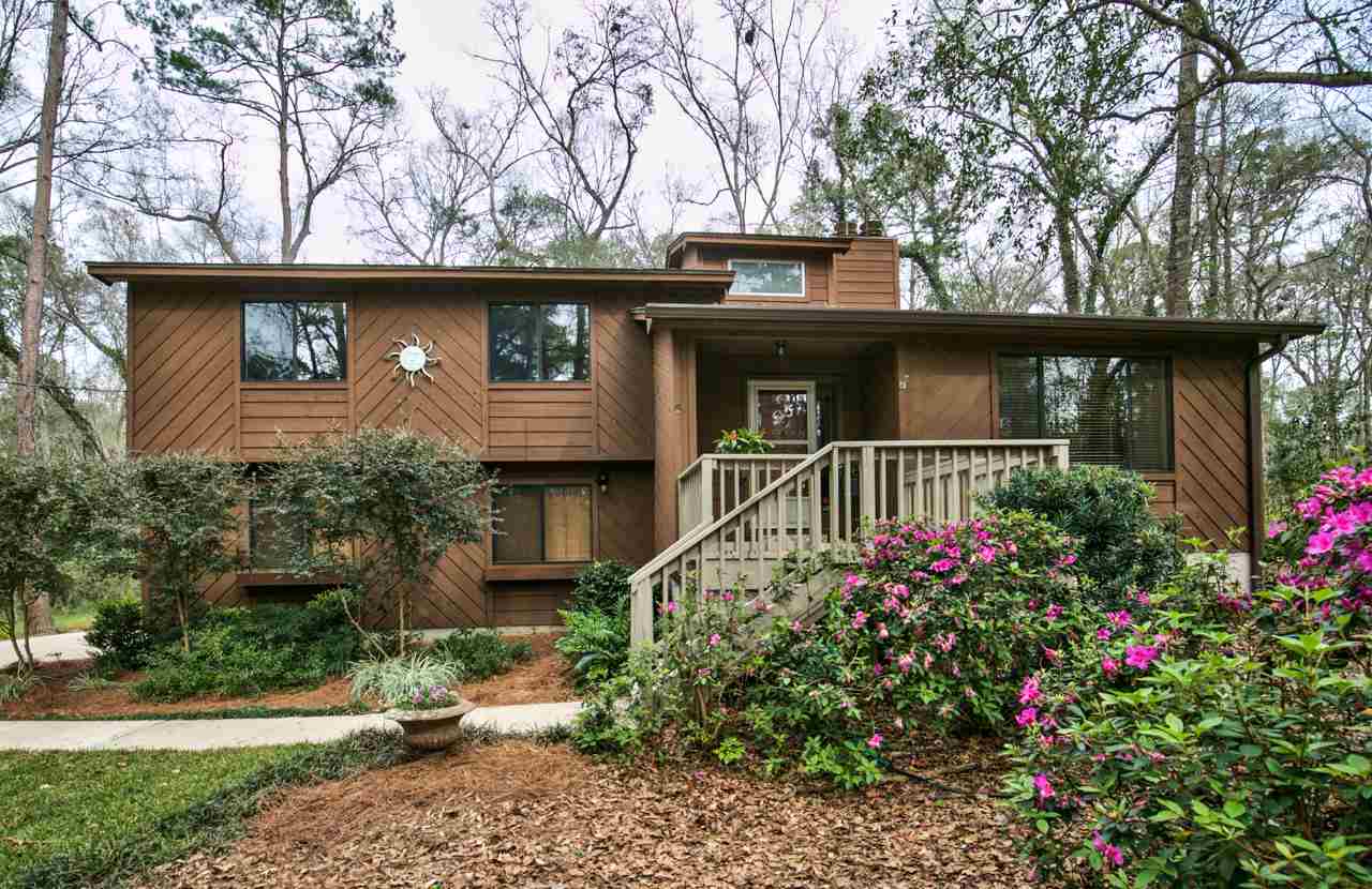 A cozy home nestled in the woods featuring a spacious deck and beautifully landscaped surroundings.