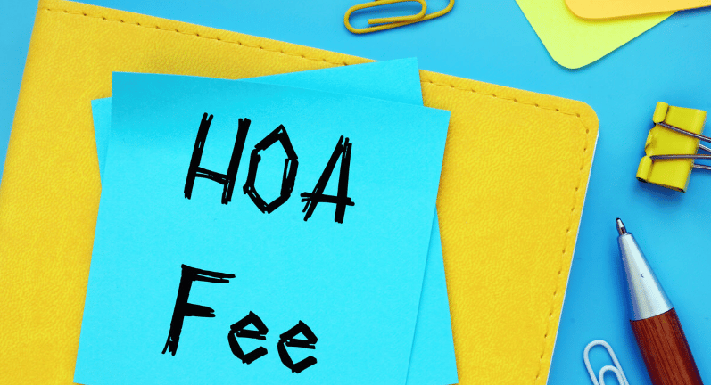 A blue note labeled “HOA Fee” on a yellow folder with office supplies.