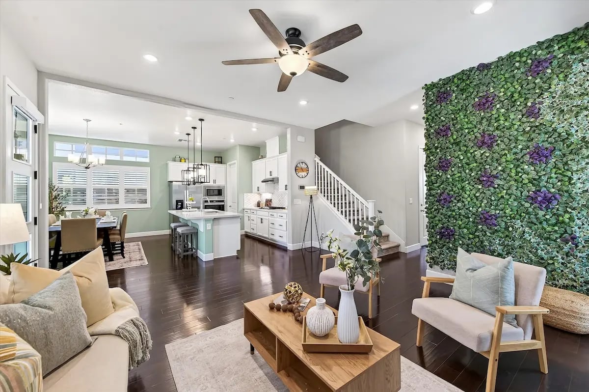 Open-plan living room and kitchen with a leafy accent wall and staircase.