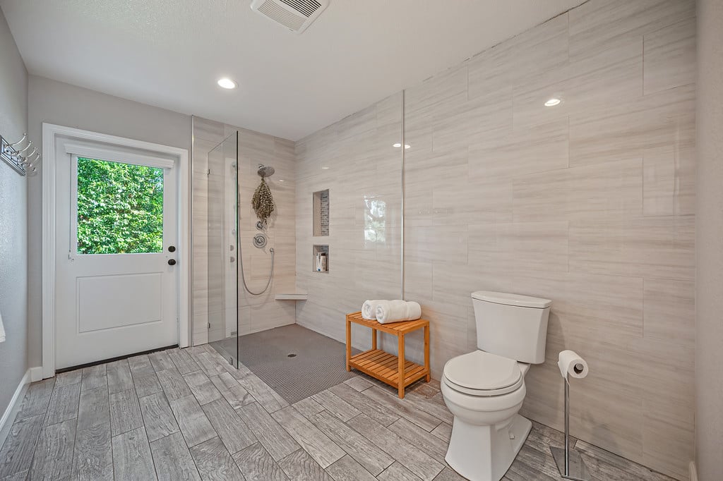 Bathroom with a glass walk-in shower, large tiled walls, and a door window overlooking greenery.