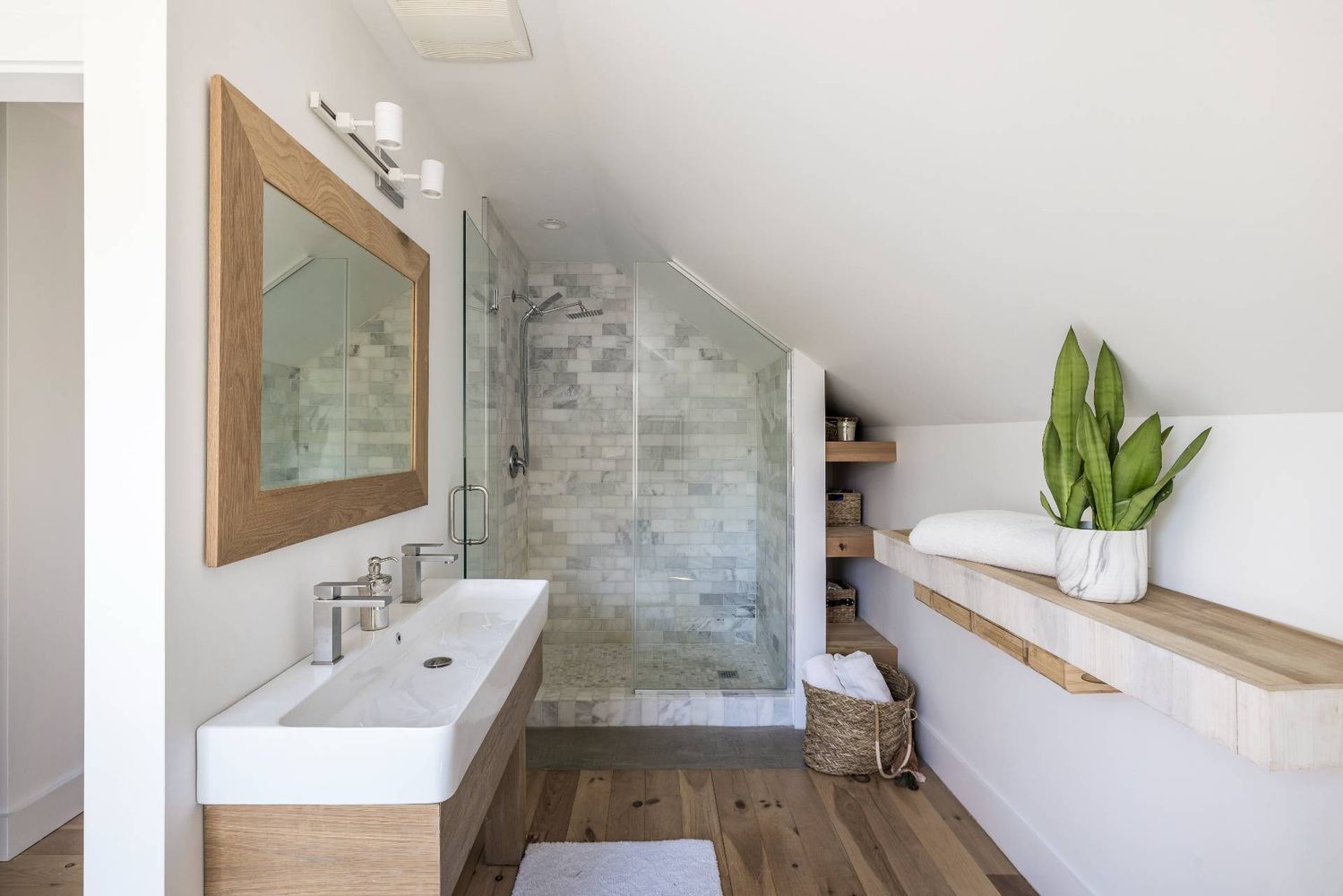 Bright bathroom with a marble-tile walk-in shower, wood vanity, and floating shelf beneath a sloped ceiling.