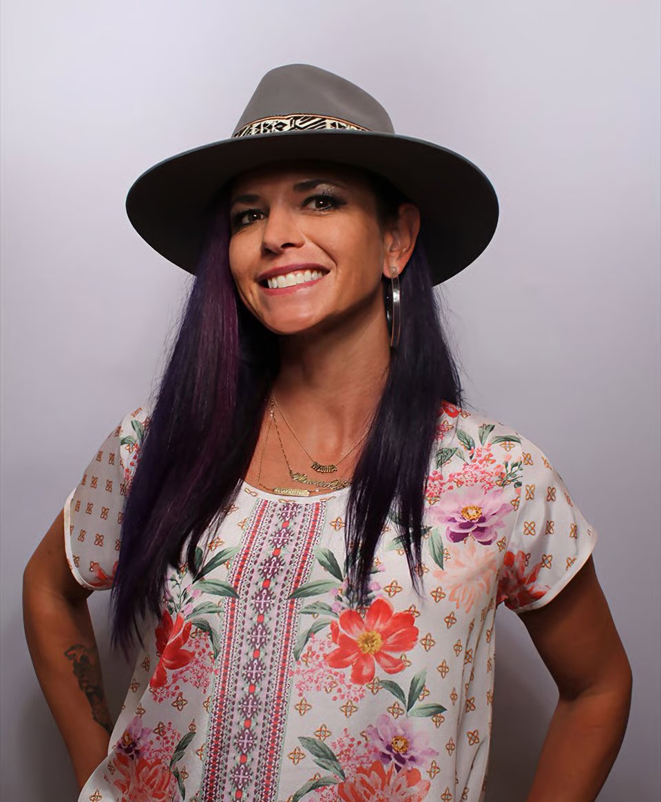 Smiling woman in a wide-brimmed hat and floral blouse.