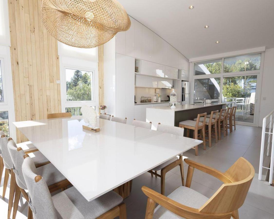 Open-plan dining room with a large white table, woven pendant light, and kitchen island.